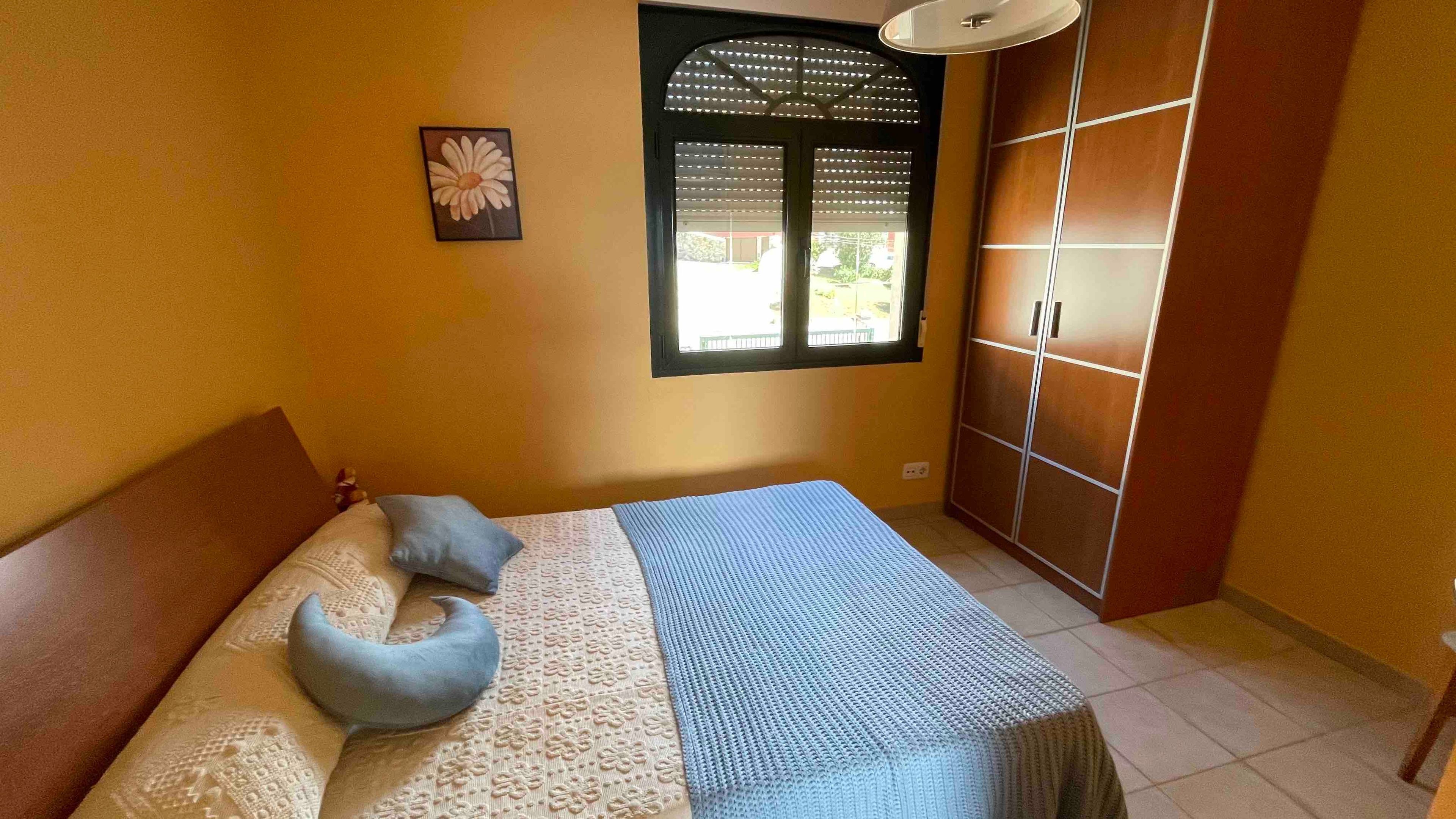 Un dormitorio con cama, almohadas, una ventana con persianas y un armario.