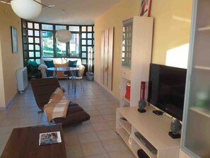 Una sala de estar moderna con un televisor de pantalla plana, un sofá, una mesa de centro y un comedor con una mesa y sillas.