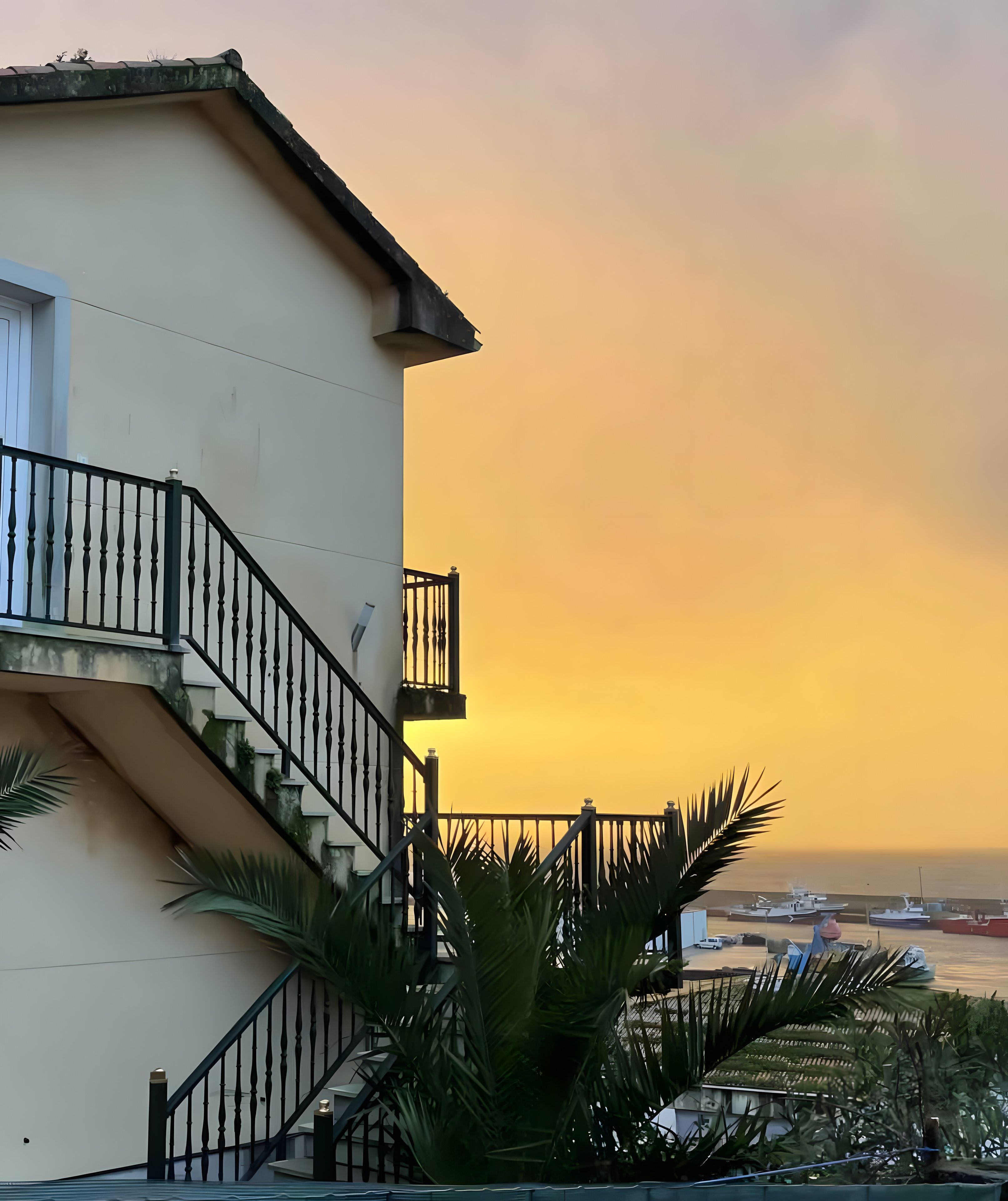 A building with a balcony, a staircase, and a view of boats at sunset.