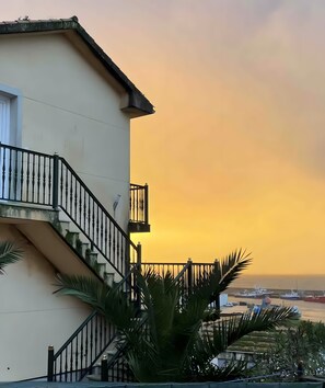 Een gebouw met balkon, wenteltrap en uitzicht op boten bij zonsondergang.