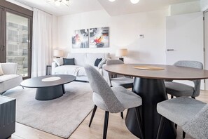 En moderne stue med et rundt spisebord, grå polstrede stole, en sofa og et stort abstrakt billede på væggen.