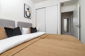 A hotel room with a bed, pillows, a wall-mounted artwork, a wardrobe, and a door with a mirror. - ZAga2C - Brand New modern apartment 200m to beach (Estepona)