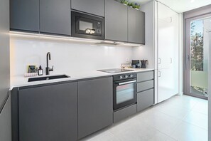 A modern kitchen with grey cabinetry, a built-in microwave, a stove, and a large window offering a view of the outdoors. - ZAga2C - Brand New modern apartment 200m to beach (Estepona)