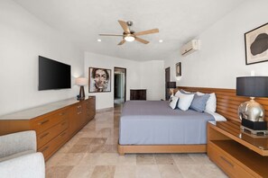 A modern bedroom with a bed, a TV, a ceiling fan, and a wooden dresser. - Stunning Ocean Views • 2BR above Zona Romantica (Puerto Vallarta)