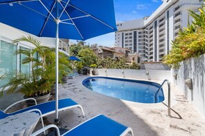 A swimming pool with lounge chairs and umbrellas, surrounded by buildings and greenery. - Stunning Ocean Views • 2BR above Zona Romantica (Puerto Vallarta)