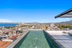 Ein Pool auf dem Dach mit Blick auf die Stadtlandschaft, einschließlich Gebäude und eines Gewässers.