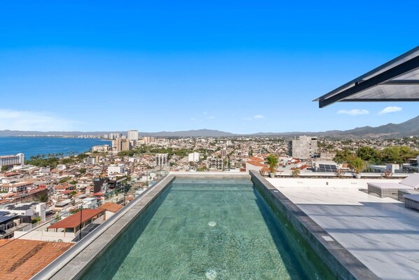 Piscina no terraço com vista para a paisagem urbana, incluindo edifícios e um corpo de água.