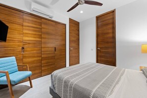 Ein Schlafzimmer mit einem Bett, einem Sessel, Holzschränken, einem Deckenventilator und einem an der Wand befestigten Fernseher.