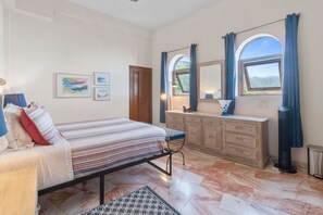 Ein Schlafzimmer mit einem Bett, einem Schminktisch, einem Stuhl und einem Fenster mit Vorhängen.