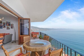 Ein Balkon mit einem runden Holztisch und Stühlen, mit Blick auf ein Gewässer.