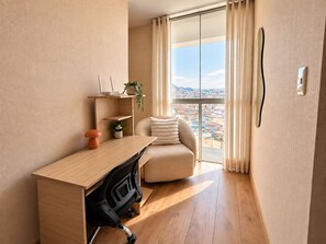 A modern room with a wooden desk, a cushioned chair, a radiator, and a view of a cityscape through large windows. - North Lima Skyline -24th floor Panoramic view (Independencia)