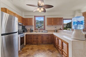 A kitchen with a stainless steel refrigerator, wooden cabinets, a built-in oven, a microwave, a coffee maker, a water dispenser, and a view of the outside. - Tranquil Two Bedroom Condo in Zona Romantica (Puerto Vallarta)