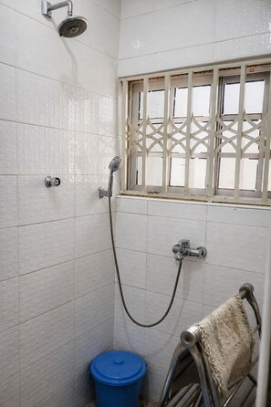 Ein Badezimmer mit weißen Fliesenwänden, einer Dusche inklusive Handbrause, einem Fenster mit dekorativem Gitter und einem Handtuchhalter mit Handtuch.