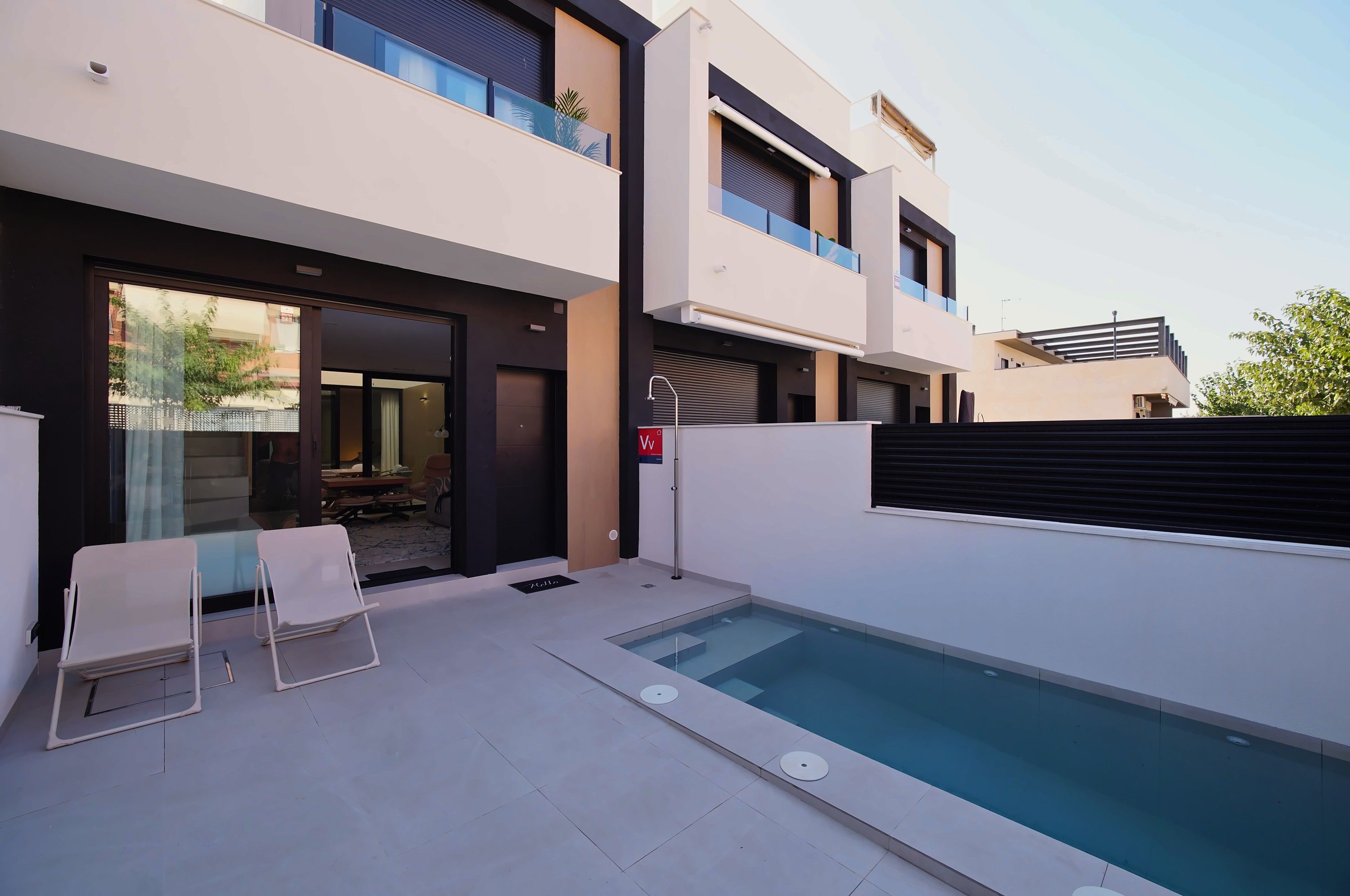 A modern two-story building with a swimming pool, a covered patio, and a glass door leading to the interior.
