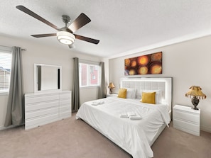 A bedroom with a bed, a ceiling fan, a dresser, a nightstand, and a painting. - Bright Home: Furnished Patio, Fast WiFi & Parking (Brampton)