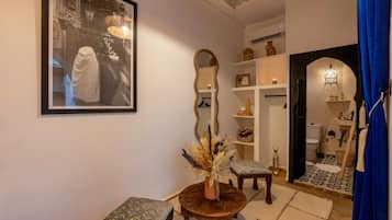 A room with a large framed photograph, a round wooden table with a vase, a patterned bench, and a mirror on the wall.