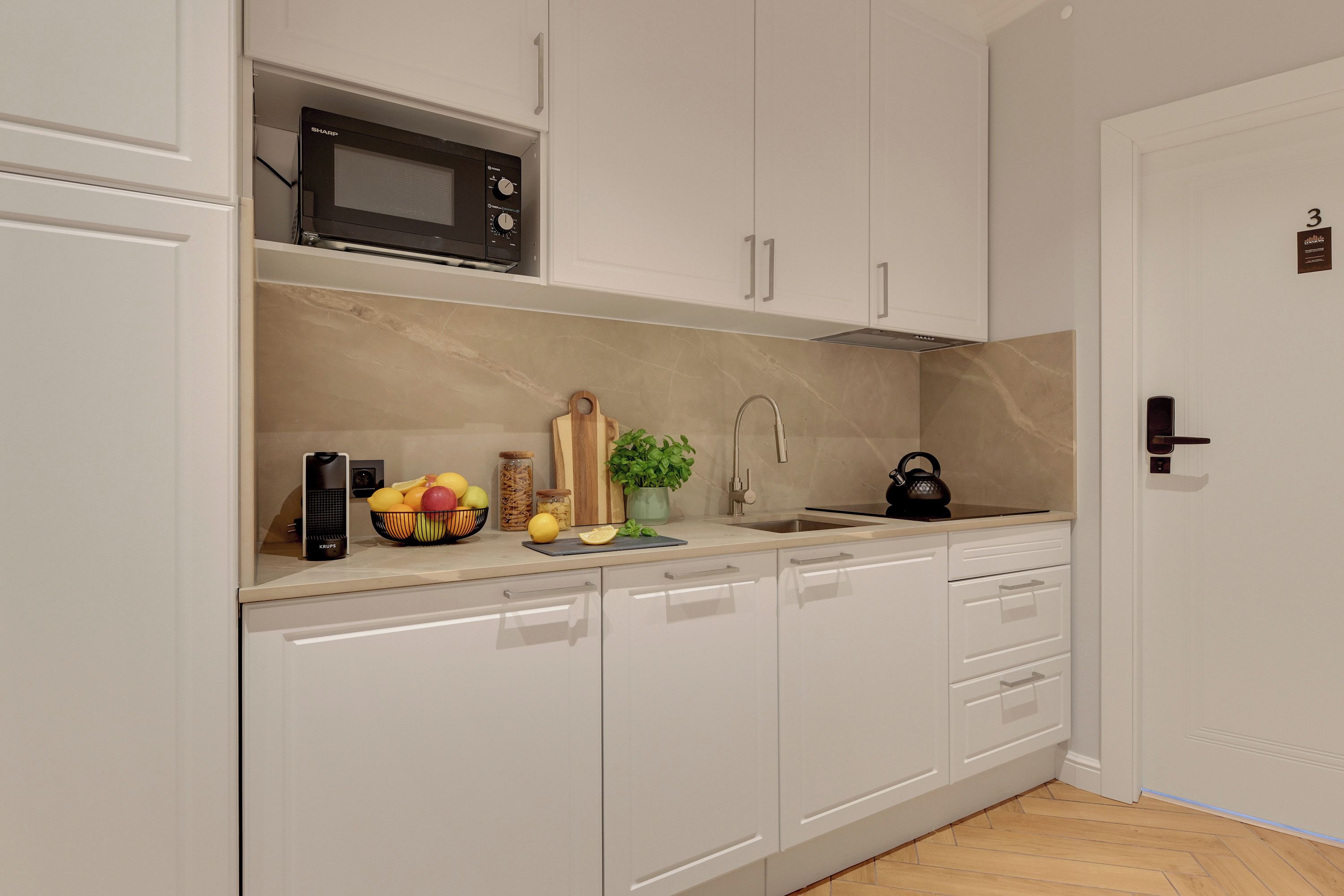 Una cocina moderna con armarios blancos, microondas, fregadero y hervidor.