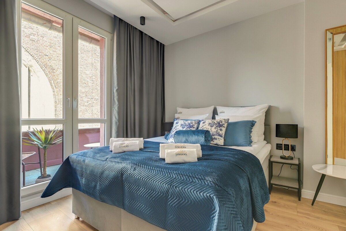 A hotel room with a large bed, a bedside table, a small table, and a window with curtains.