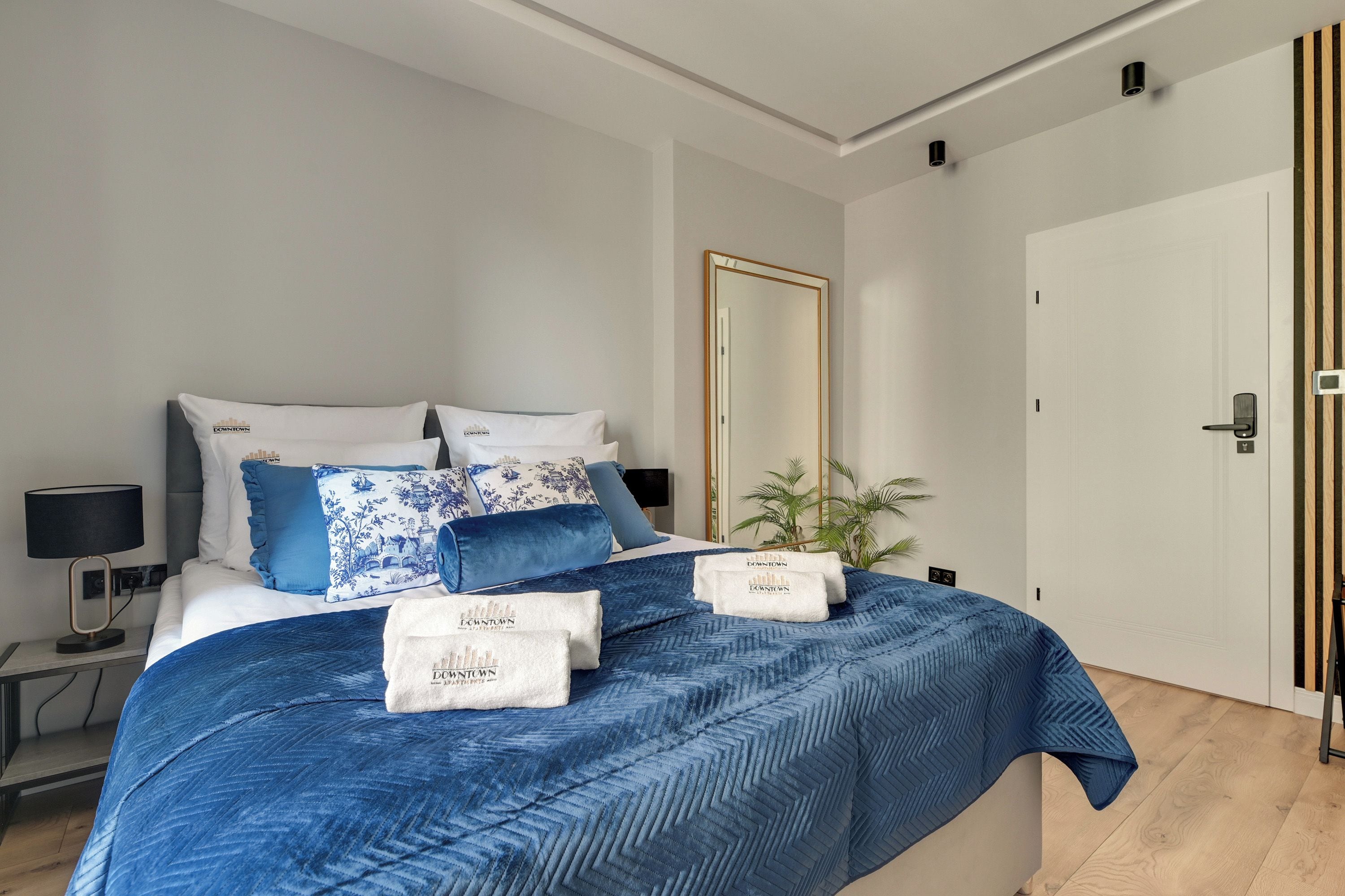 Ein modernes Hotelzimmer mit einem großen Bett, einem Nachttisch, einer Lampe, einem Spiegel und einer Tür mit einer vertikalen Holzverkleidung.