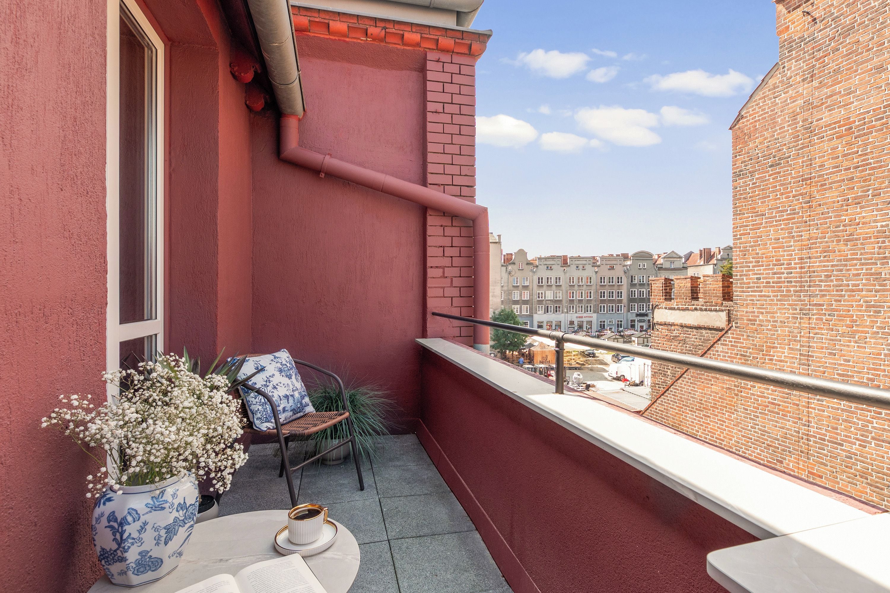Ein Balkon mit Blick auf eine Stadtlandschaft, ein Tisch mit Tasse und Untertasse sowie ein Sessel mit Kissen.