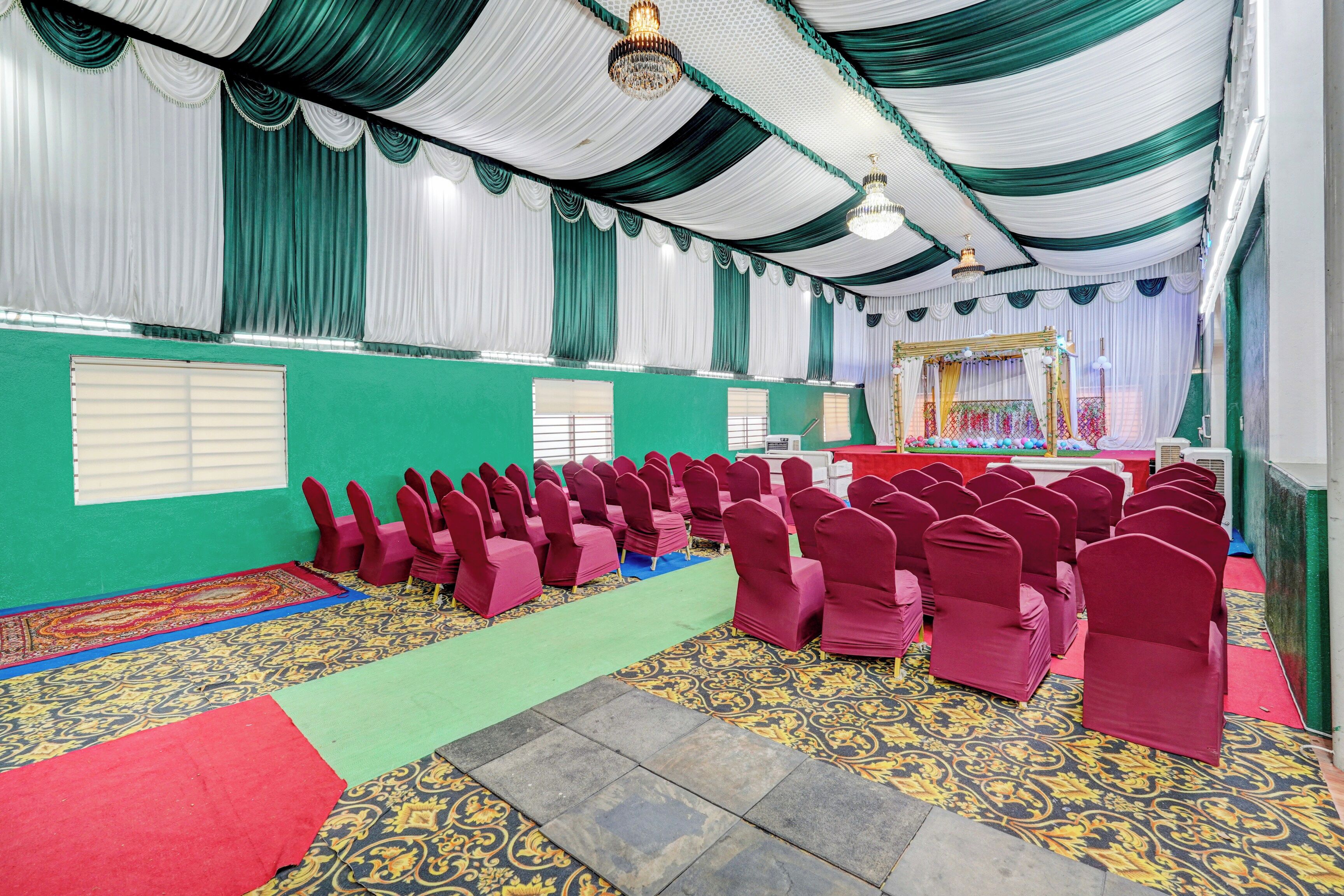 A hall with rows of chairs, a stage with a backdrop, and a patterned carpet.