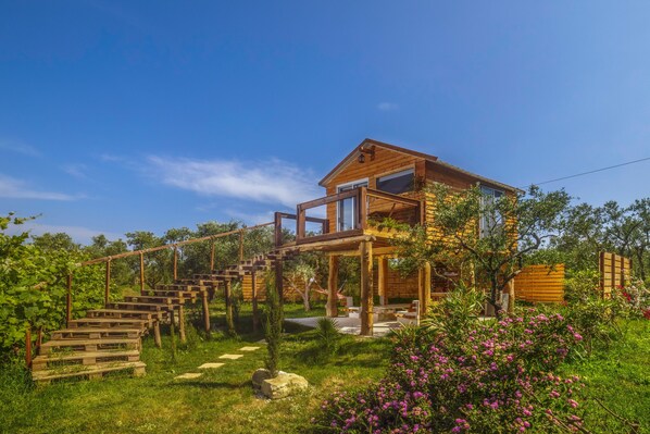 Una casa di legno con un balcone, immersa in un giardino ricco di piante e fiori.