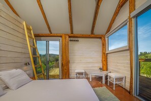 Una camera da letto con un letto, una scrivania e una sedia, travi a vista sul soffitto e una grande finestra.