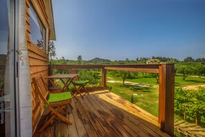 Une terrasse en bois avec une table et des chaises, donnant sur un paysage verdoyant.