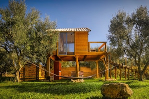 Ein hölzernes Baumhaus mit Balkon, umgeben von Bäumen und Gras.