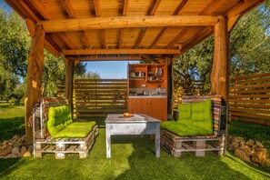 Eine hölzerne Pergola mit integrierter Küchenzeile, einem Tisch und Stühlen sowie Blick auf die umliegende Landschaft.