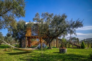 Une cabane en bois dotée d’un balcon, entourée d’oliviers et agrémentée d’un hamac.