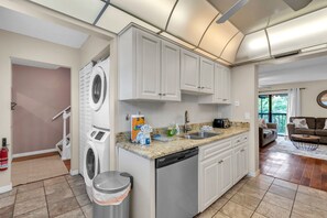 Une cuisine moderne dotée d’un lave-linge et d’un lave-vaisselle intégrés, d’un plan de travail en granit et donnant sur l’espace de vie.