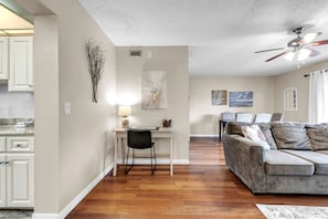 A modern living room with a grey sofa, a dining area with a white table and chairs, and a kitchen with white cabinets. - Fishing Pier | Heated Community Pool | Quick Walk to the Beach | Sea Shell #32 (Indian Shores)