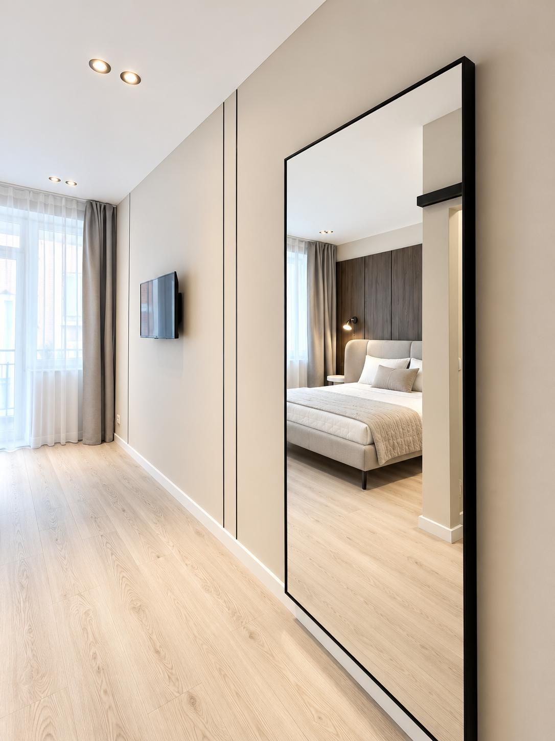 Une chambre d’hôtel moderne équipée d’un grand miroir, d’un lit, d’une table de chevet et d’un téléviseur à écran plat.