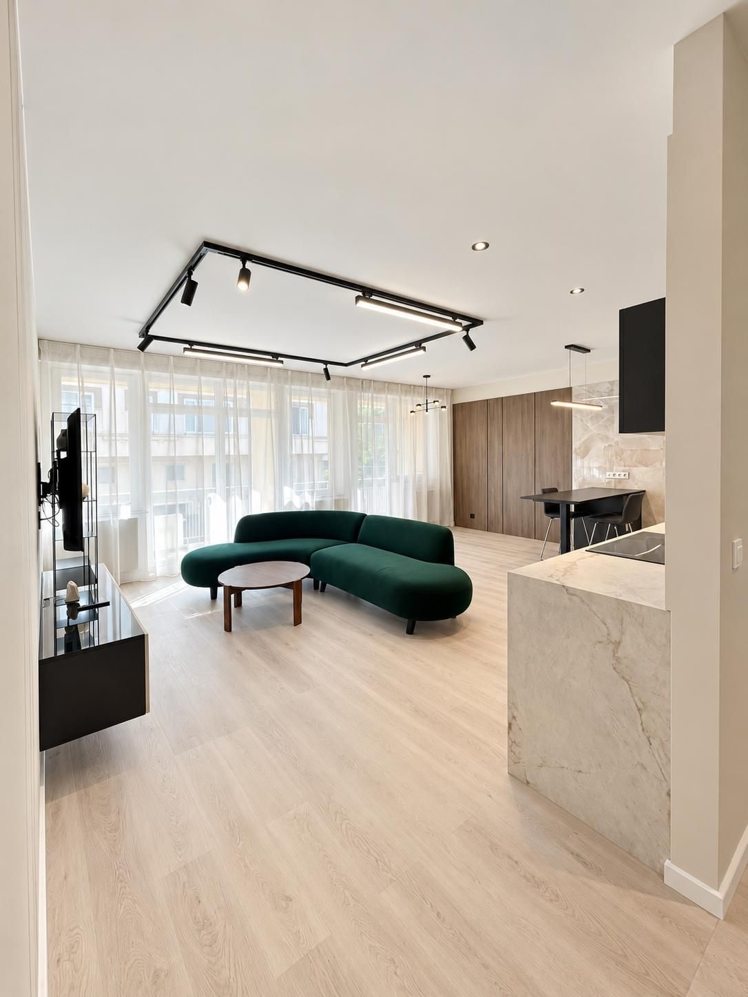Un salon moderne avec un canapé d’angle, une table basse et un coin cuisine doté d’un plan de travail en marbre.