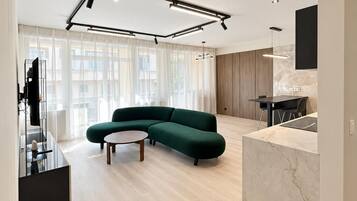 Un salon moderne avec un canapé d’angle, une table basse et un coin cuisine doté d’un plan de travail en marbre.