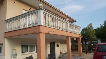 A two-story building with a balcony, outdoor seating, and a red car parked nearby.