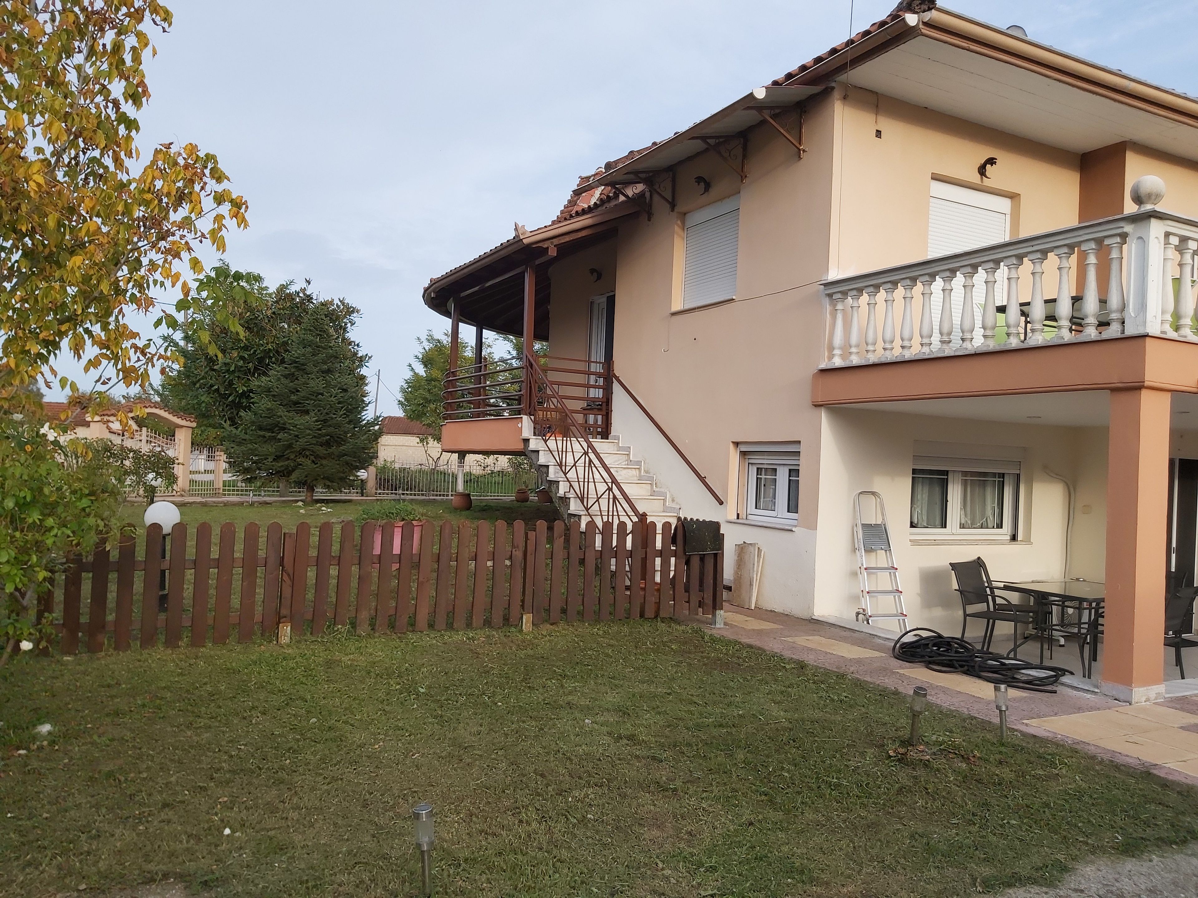 A two-story residential building with a balcony, a staircase, and a fenced yard.
