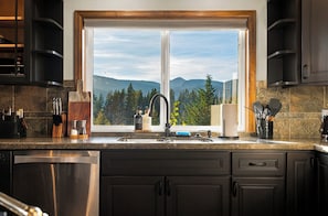 A kitchen with a large window, granite countertops, and dark cabinetry. - Elkai Lodge | Mt. Rainier View + Hot Tub (Packwood)