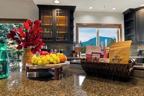 A kitchen counter with a fruit platter, a bottle, and a basket of items. - Elkai Lodge | Mt. Rainier View + Hot Tub (Packwood)