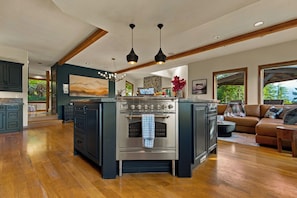 A modern kitchen with a central island, built-in oven, and a dining area with a view. - Elkai Lodge | Mt. Rainier View + Hot Tub (Packwood)