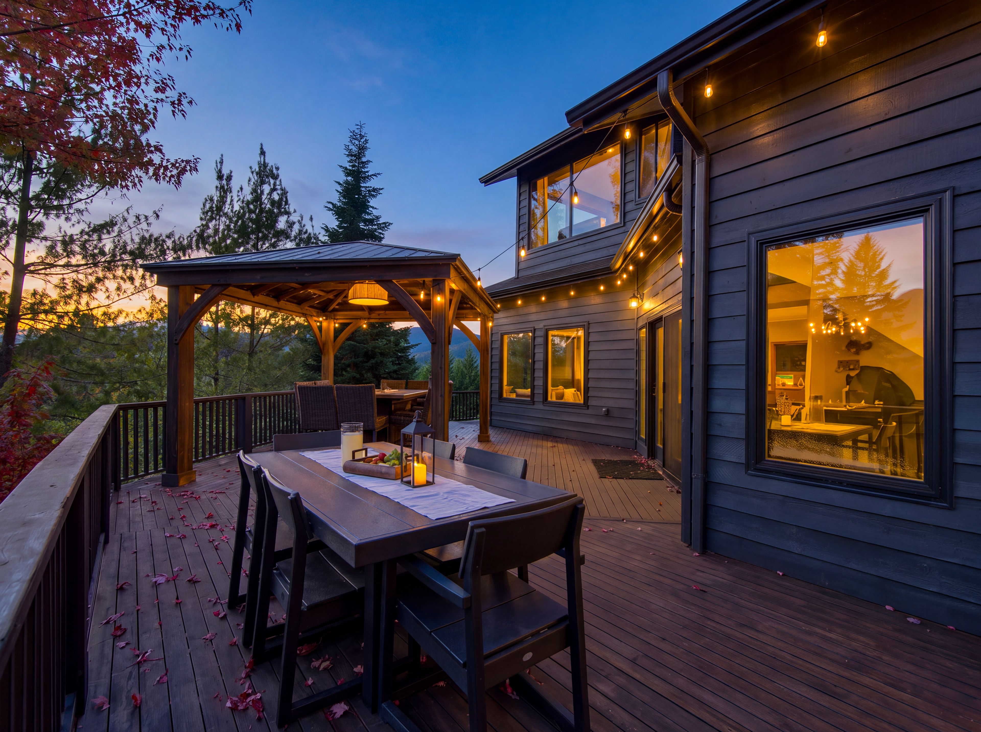 A wooden deck with a pergola, outdoor seating, and a view of a house with large windows and string lights.