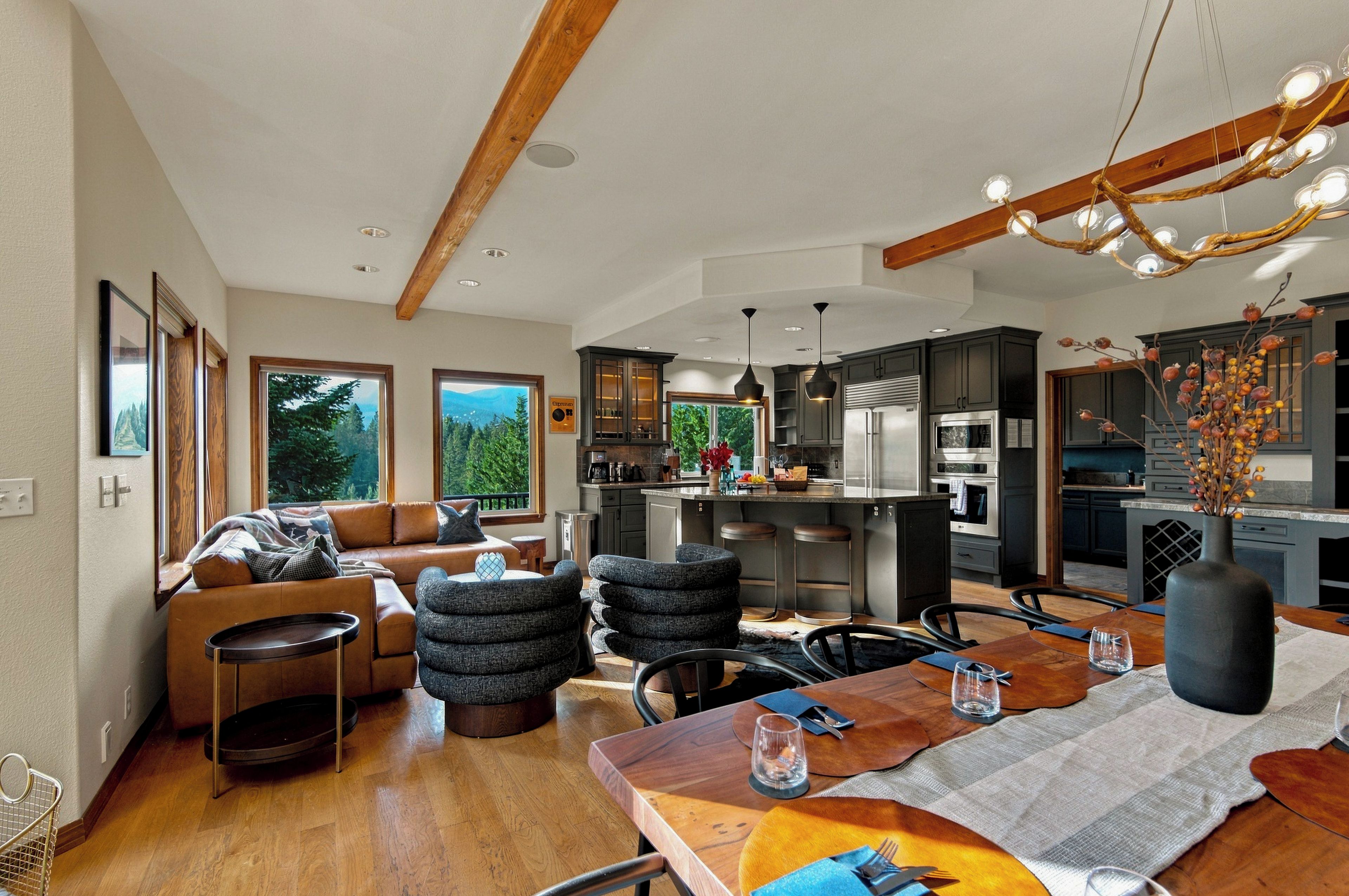 A modern kitchen with dark cabinetry, a central island, and a dining area with a wooden table and chairs.