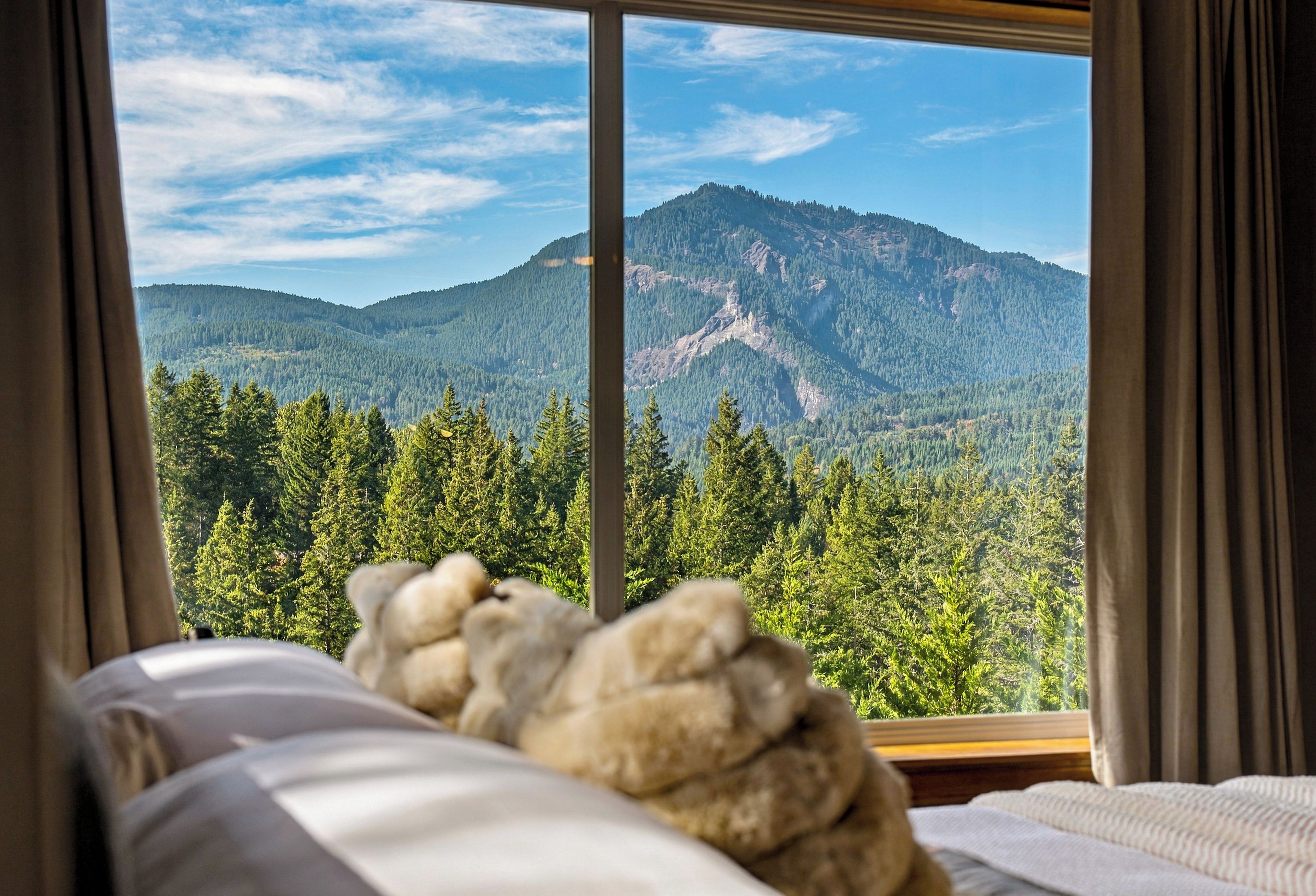 A bed with a mountain view through a window, curtains, and a pillow.
