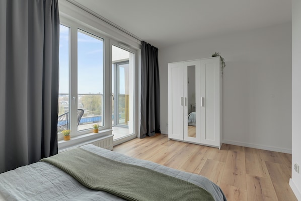 A bedroom with a large window, a bed, a wardrobe, and a view of the outdoors.