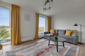 A modern living room with a grey sofa, yellow cushions, a round coffee table, and a floor lamp. - Baltic Seaside Letnica with Parking (Gdańsk)