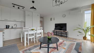 A modern living room with a dining area, kitchen, and a flat-screen TV.