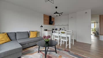 Ein modernes Wohnzimmer mit einem grauen Ecksofa, einem kleinen runden Tisch mit einer Vase und einem farbenfrohen Teppich.