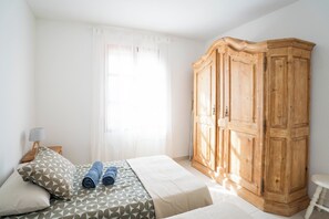 Une chambre à coucher avec un lit, une armoire, une lampe et une fenêtre avec des rideaux.