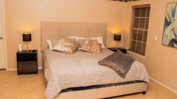 Une chambre à coucher comprenant un lit, deux tables de chevet, une fenêtre avec des stores et un mur orné d’un motif décoratif.
